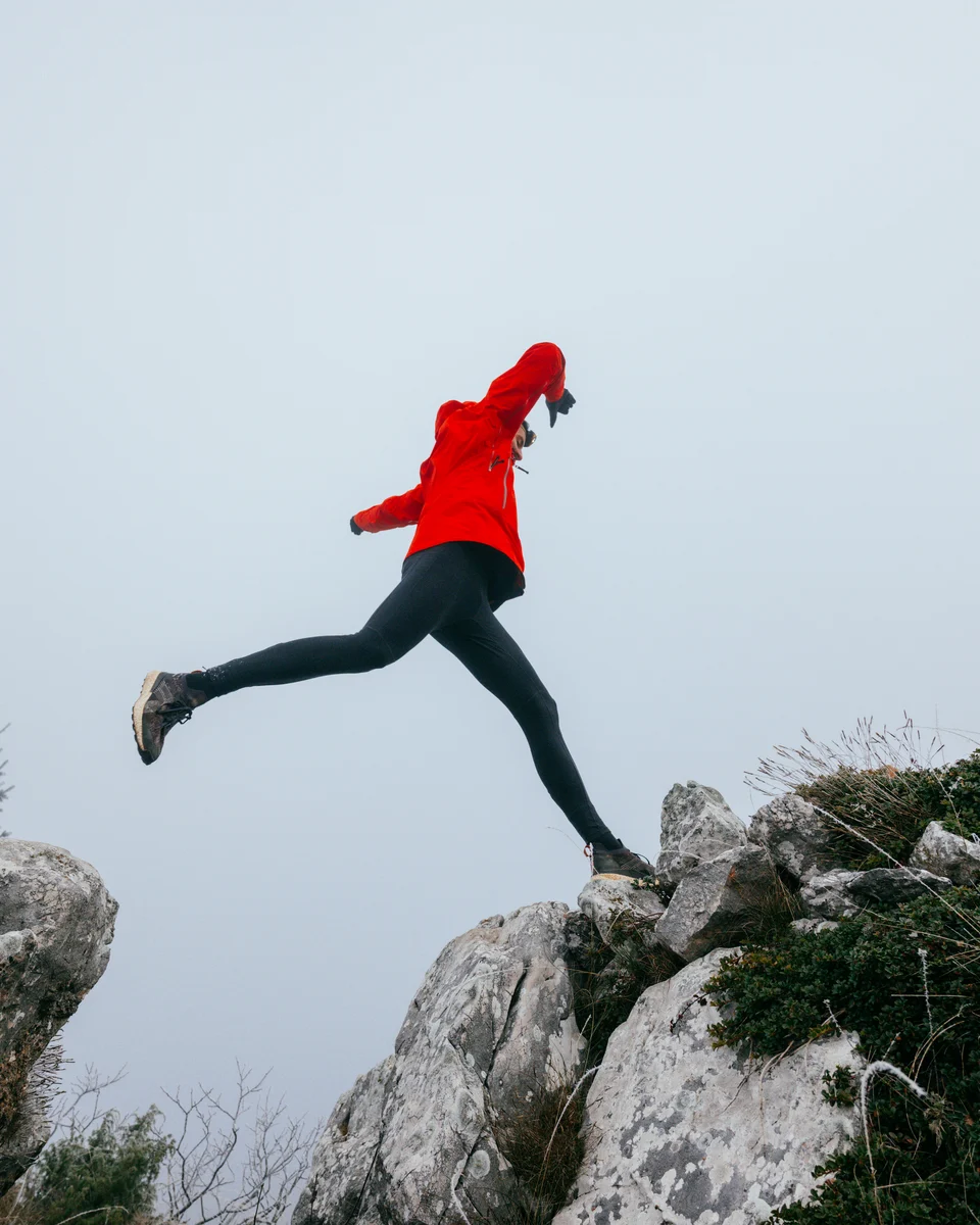 Masters runner leaping across a gap between rocks in a mountain landscape